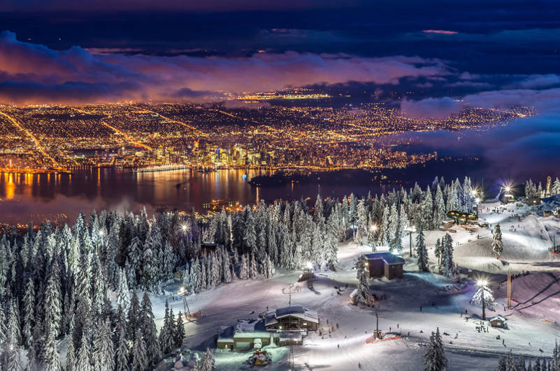 Snowy mountain top with view of Vancouver at night