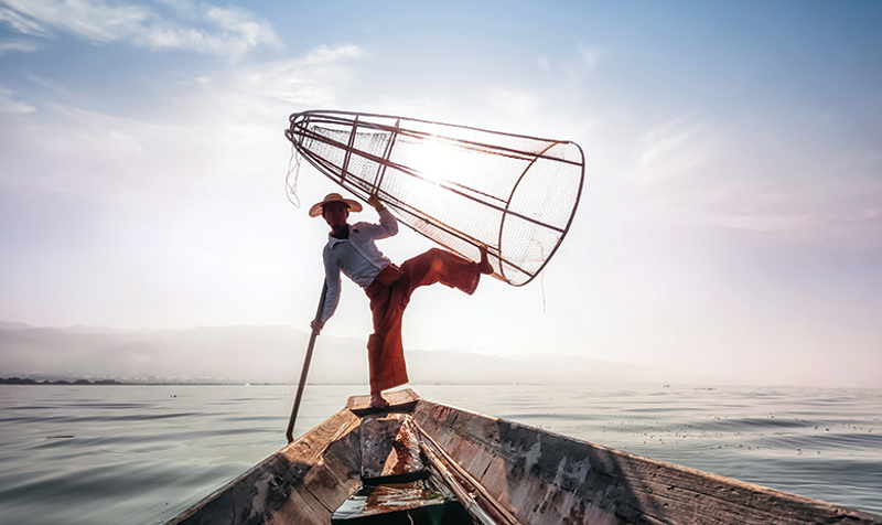 Burmese fisherman with next balanced on foot